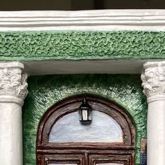 a green and white building with two large doors that have columns on each side of the door