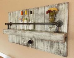 a wall mounted shelf with bottles and glasses on it, next to a vase filled with flowers