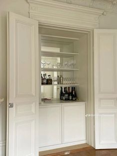 an open cabinet with wine glasses and bottles on it in a room that has wood floors