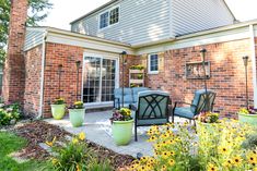 a patio with chairs and potted plants in front of a brick building on a sunny day