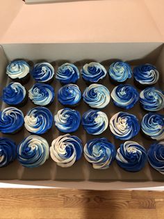 a box filled with blue and white cupcakes on top of a wooden table