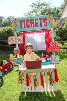 a young boy sitting at a table with a laptop in front of a ticket booth