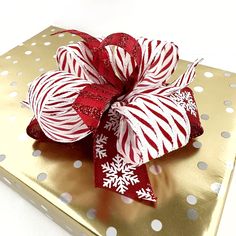 a gold gift box with red and white candy canes wrapped in ribbon on it