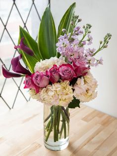 a vase filled with pink and white flowers on top of a wooden table next to a window