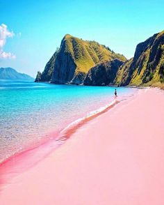 a person is walking on the beach with pink sand and mountains in the background at low tide