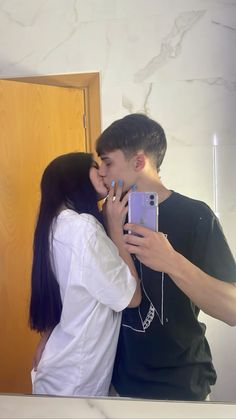 a young man and woman kissing in front of a mirror while holding their cell phones