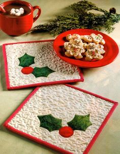 three placemats with holly designs on them next to a plate of cookies and a cup of hot chocolate