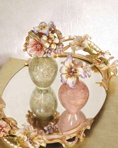 two vases with flowers are sitting on a plate that has gold trim around it