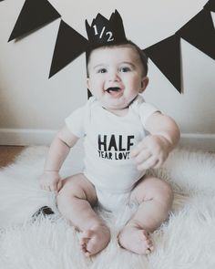 a baby is sitting on the floor wearing a black and white shirt that says half year love