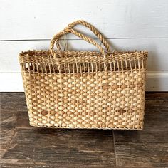 a woven basket sitting on top of a wooden floor next to a white painted wall