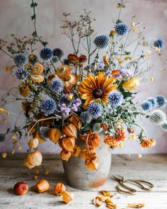 a vase filled with lots of different colored flowers on top of a wooden table next to scissors