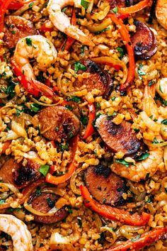 a plate full of shrimp and rice with sausages, carrots, and peppers