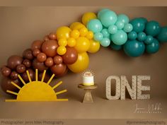 a birthday cake with balloons and the word one on it in front of a backdrop