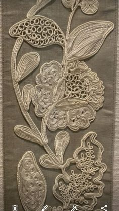 an embroidered piece with flowers and leaves on it's side, hanging from a wall