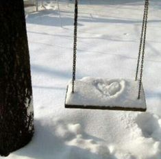 a swing that is in the snow next to a tree with a heart drawn on it