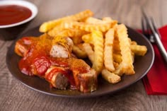 a plate topped with french fries and meat covered in sauce next to a bowl of ketchup