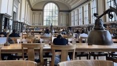 people are sitting at desks in the library with bookshelves and large windows