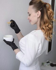 a woman wearing black gloves is holding a bowl and spoon in one hand while looking at the wall