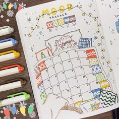 an open planner with markers and pens next to it on a wooden table covered in snowflakes