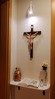 a crucifix is mounted on the wall above a shelf with flowers and an open book