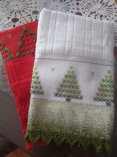 two red and white towels with christmas trees on them sitting on a table next to doily