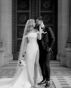 a bride and groom kissing in front of an ornate doorway at their wedding day, black and white photo