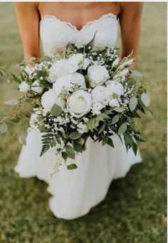 a bride holding a bouquet of flowers in her hand on the grass at their wedding