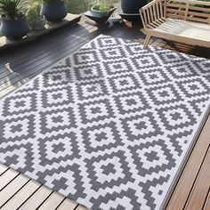 an outdoor area rug on a deck with potted plants and wooden benches in the background