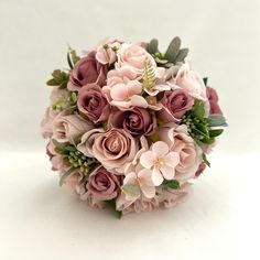 a bridal bouquet with pink flowers and greenery on the top is sitting on a white surface