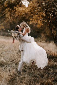 a bride and groom kissing in an open field with tall grass, trees and yellow leaves