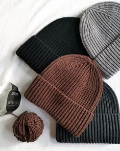 three beanies are laying next to each other on a white sheet, one is brown and one is black