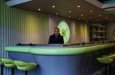 a man sitting at a bar in front of a green and blue counter with stools