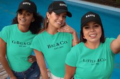 three women wearing matching green shirts and black caps pose in front of a swimming pool