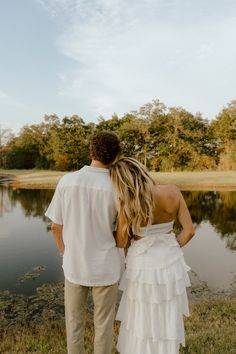 a man and woman standing next to each other in front of a lake