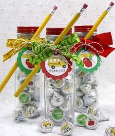 three glass jars filled with candy and two yellow pencils in each jar, one has a green ribbon on the top