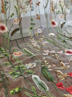 an embroidered fabric with flowers and leaves on the side, in front of a window