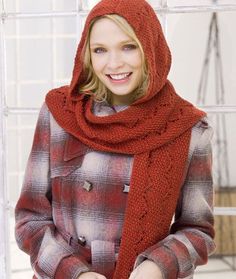 a woman wearing a red knitted scarf and jacket with buttons on the collar, standing in front of a white wall