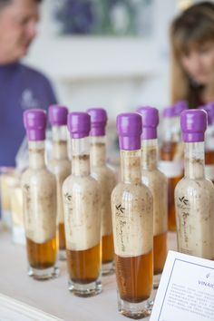 bottles filled with liquid sitting on top of a table next to a woman in a blue shirt