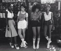 three women standing next to each other in front of a metal fence with their legs crossed