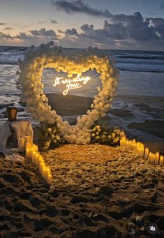 a heart shaped sign with candles on the beach