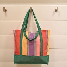 a multicolored tote bag hanging on a hook in front of a white wall