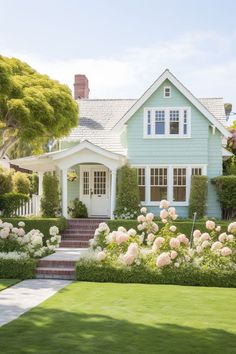 a blue house with white trim and flowers in the front yard is surrounded by greenery