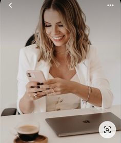 a woman sitting at a table looking at her cell phone and holding a coffee cup