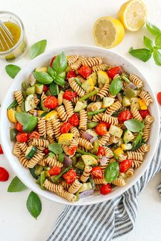 a white bowl filled with pasta salad next to sliced lemons