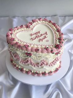 a heart - shaped cake with pink and white frosting on a tableclothed surface