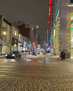 a city street at night with cars parked on the side walk and people walking down the sidewalk