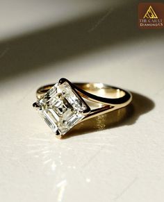 an engagement ring with a princess cut diamond in the center, on a white surface