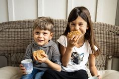 two children sitting on a couch eating donuts