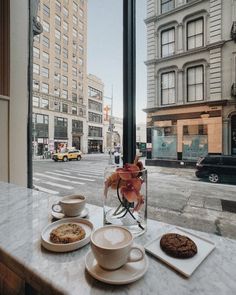 a table with plates and cups on it in front of a window overlooking the street