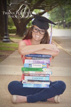 a young woman sitting on the ground with her graduation cap on top of some books